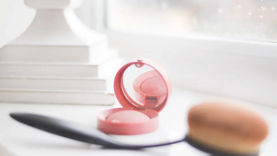 Blush rosa e pennello appoggiati su un tavolo chiaro